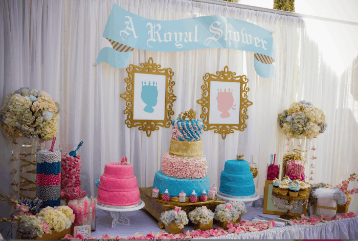 A royal-themed baby shower dessert table in a NY party hall Brooklyn, featuring a blue and gold cake, pink and blue cakes, framed silhouettes, flowers, and candy jars beneath a banner reading "A Royal Shower.